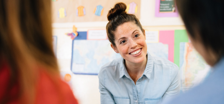 Junge Lehrerin sitzt in einem Klassenzimmer und lächelt ihre Schülern an. | make & mint - mintLab Fehler zelebrieren